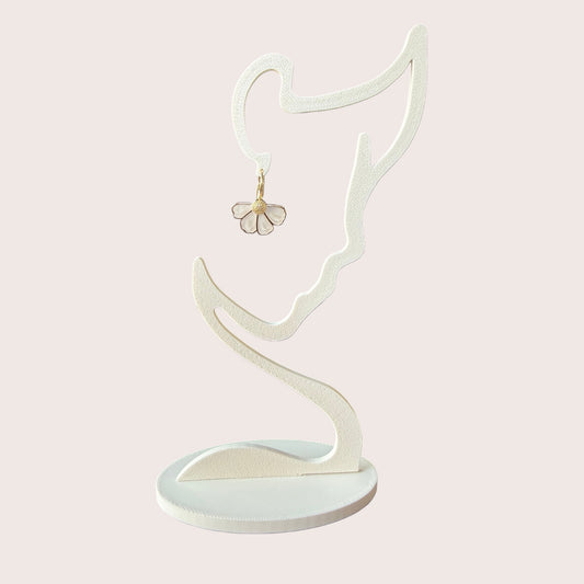 Nitelief bloem flower-shaped earring with white petals and gold center hanging on a minimalist face-shaped stand