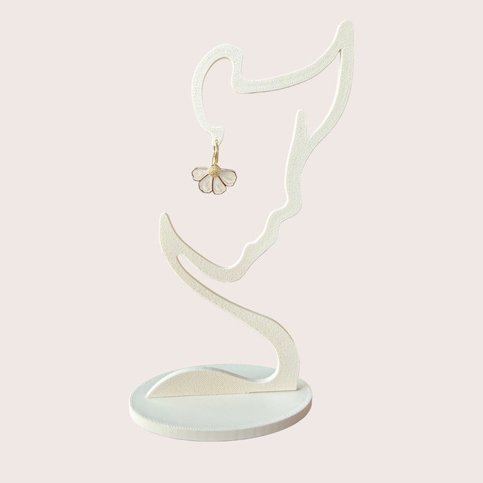 Nitelief bloem flower-shaped earring with white petals and gold center hanging on a minimalist face-shaped stand