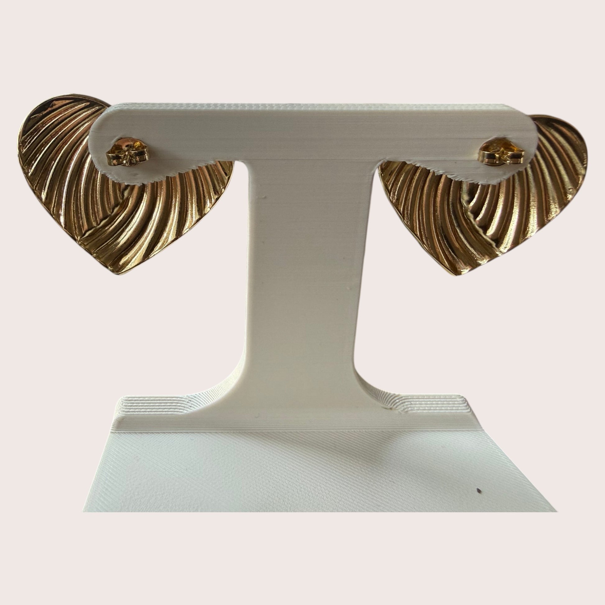 Nitelief CONCEPT golden heart earrings with a ribbed texture displayed on a white stand
