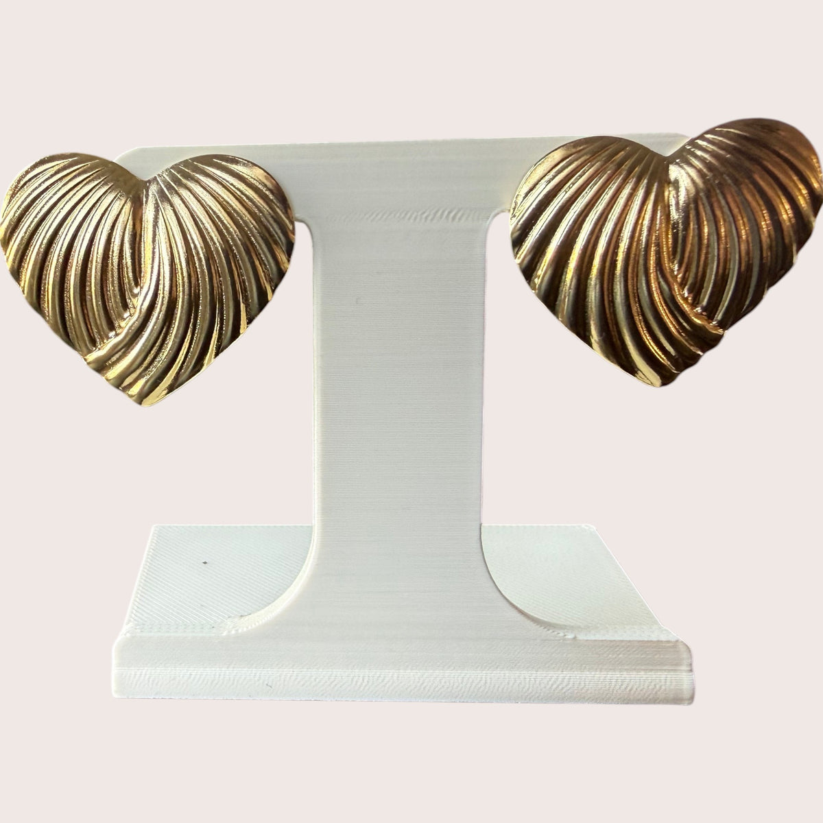 Nitelief CONCEPT golden heart earrings featuring a ribbed, textured design on a white display stand.