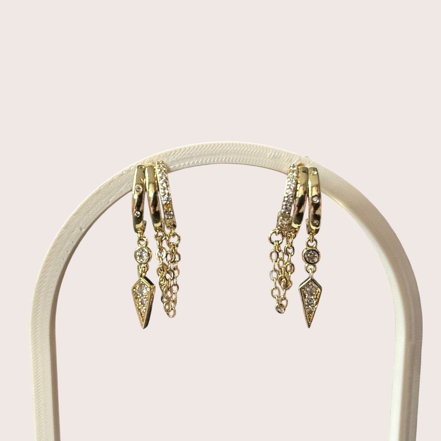 Nitelief gold hoop earrings with dangling chains and diamond-like stone accents on a display stand