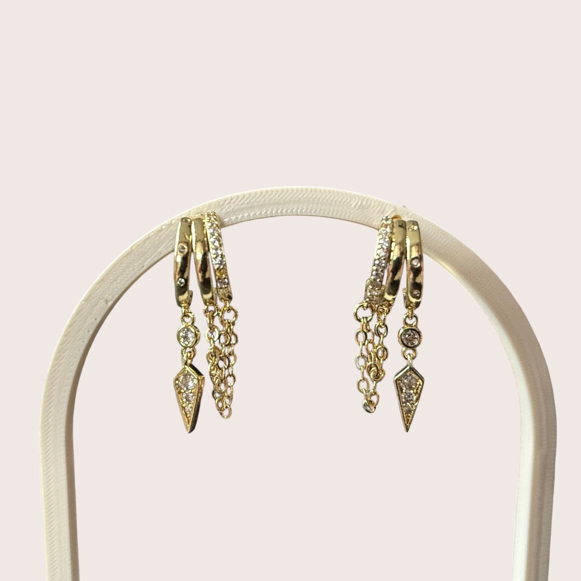 Nitelief gold hoop earrings with dangling chains and diamond-like stone accents on a display stand