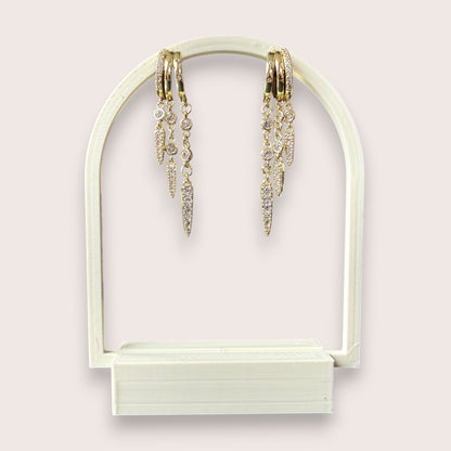 Nitelief gold hoop earrings with dangling crystal-encrusted spike charms on a white arched display stand.