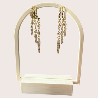 Nitelief gold hoop earrings with dangling crystal-encrusted spike charms on a white display stand