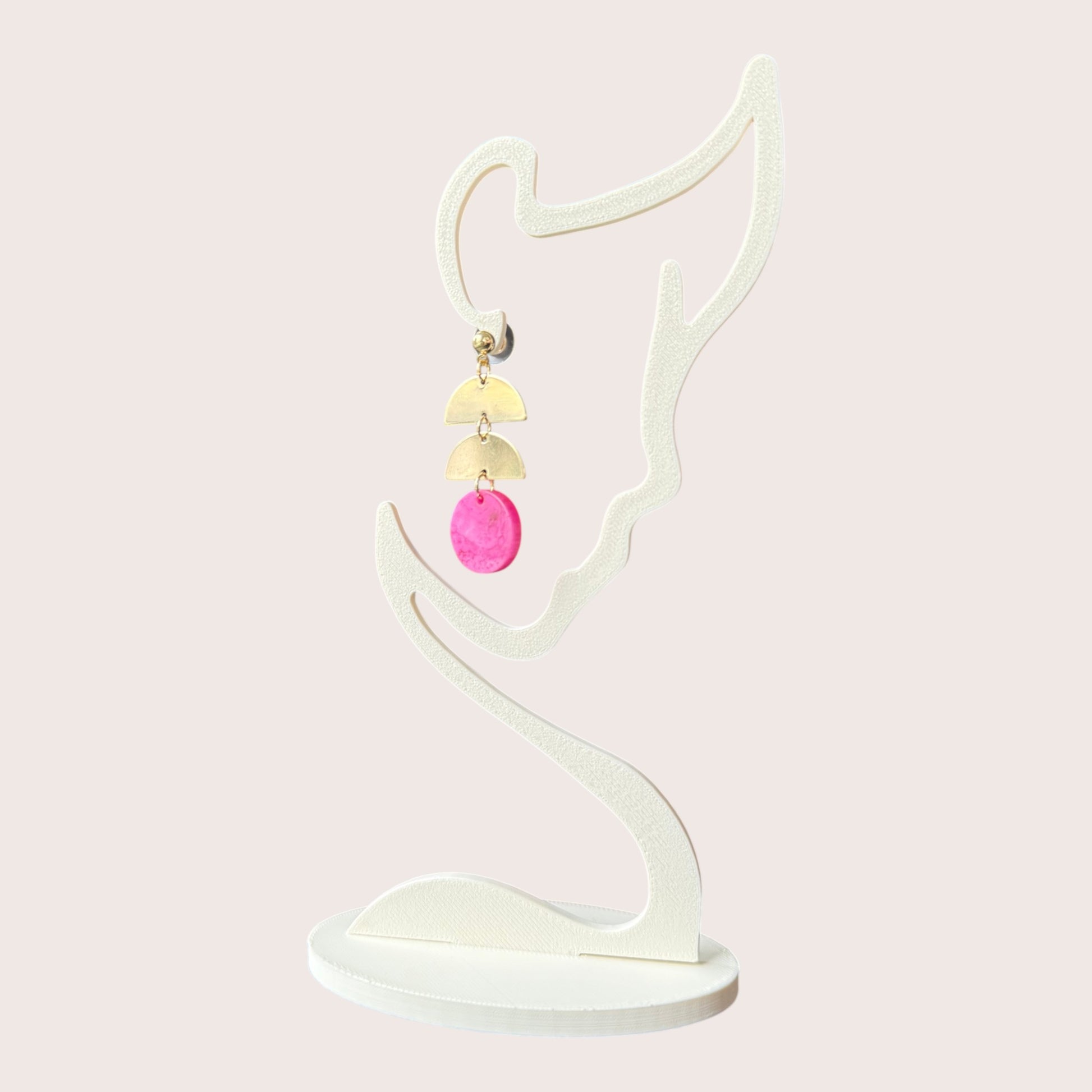 Nitelief gold and bright pink dangle earrings featuring geometric semi-circle and circle shapes on a display stand
