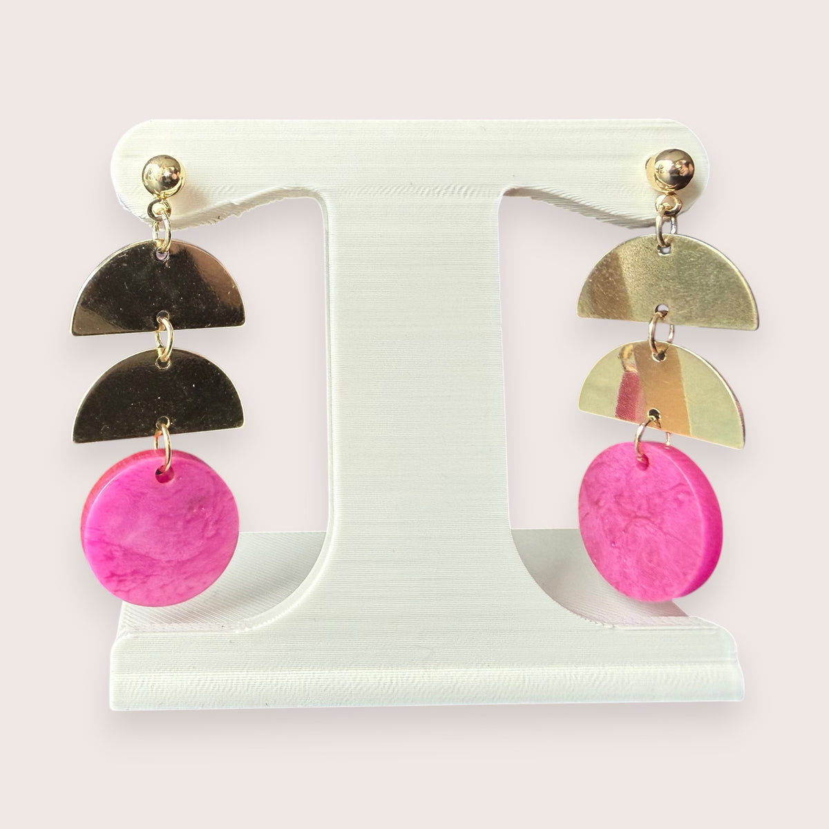 Nitelief gold-tone metal and pink circular resin dangle earrings on a white display stand
