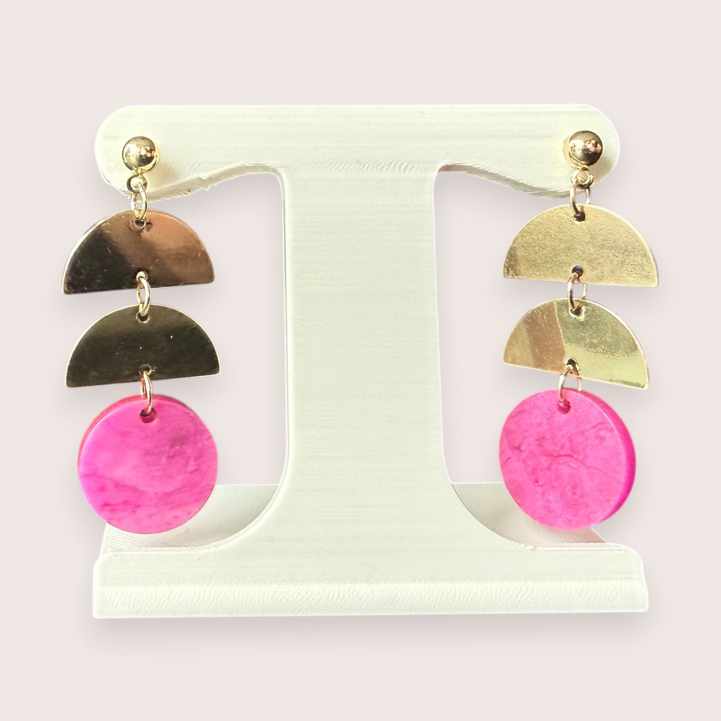Nitelief gold-tone metal semi-circle and pink circular resin drop earrings displayed on a white stand