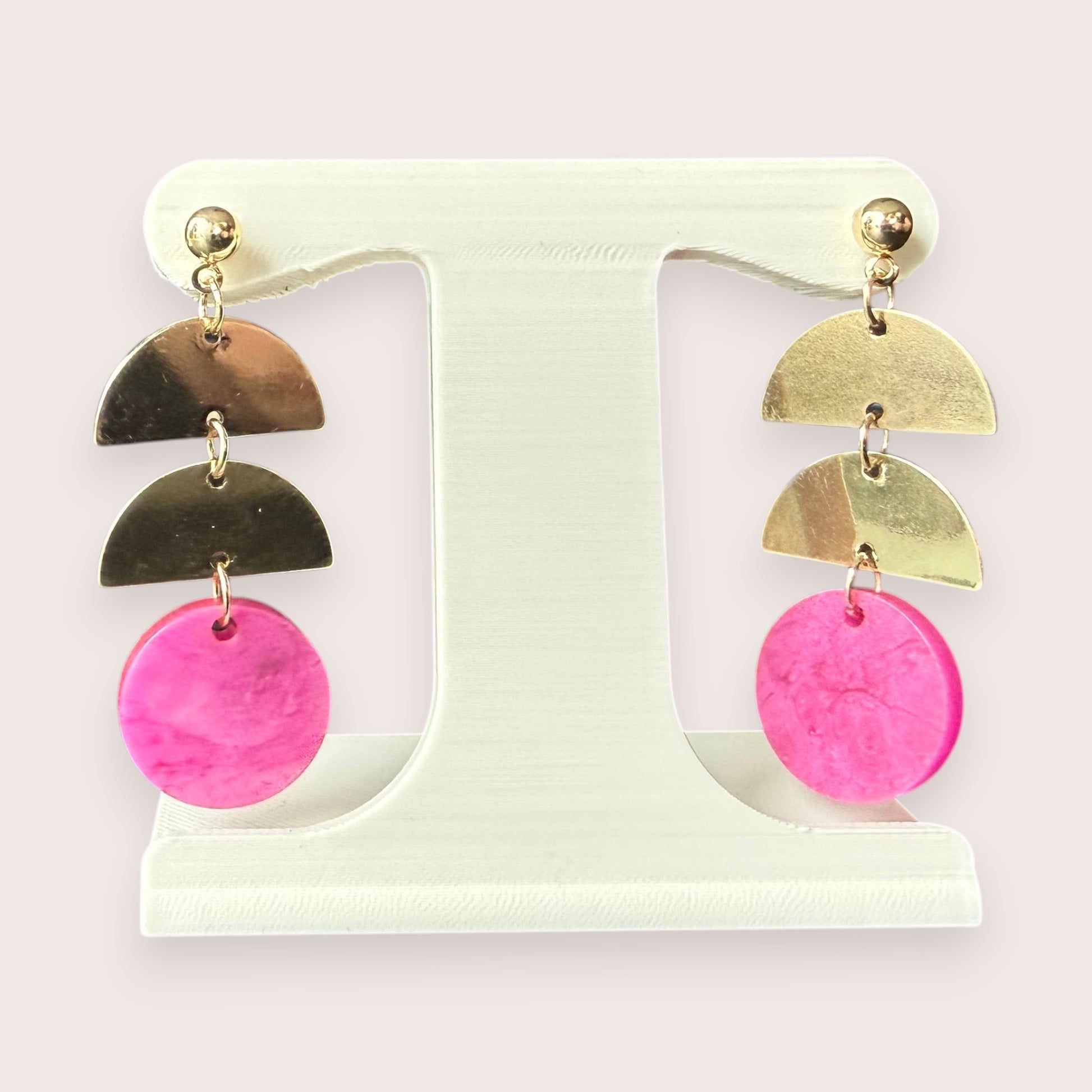 Nitelief gold-tone metal semi-circle and pink circular resin drop earrings displayed on a white stand