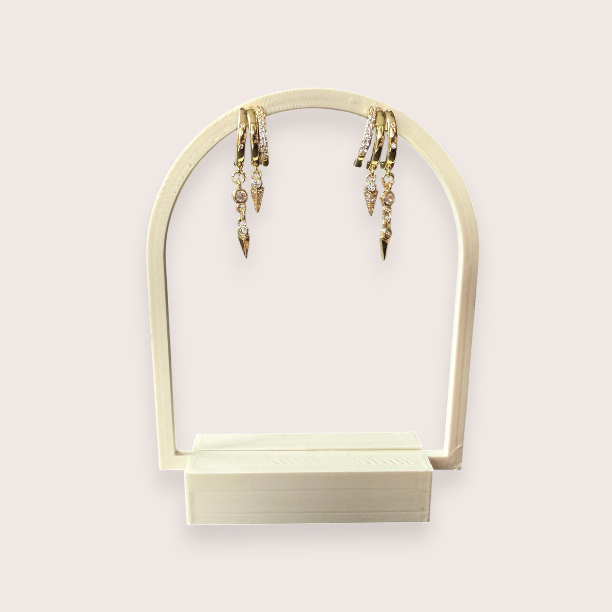 Nitelief gold hoop earrings with dangling crystal-encrusted spike charms displayed on an arched stand.