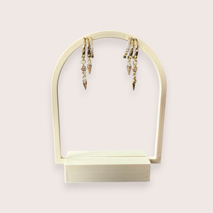 Nitelief gold hoop earrings with dangling crystal-encrusted spike charms displayed on an arched stand.