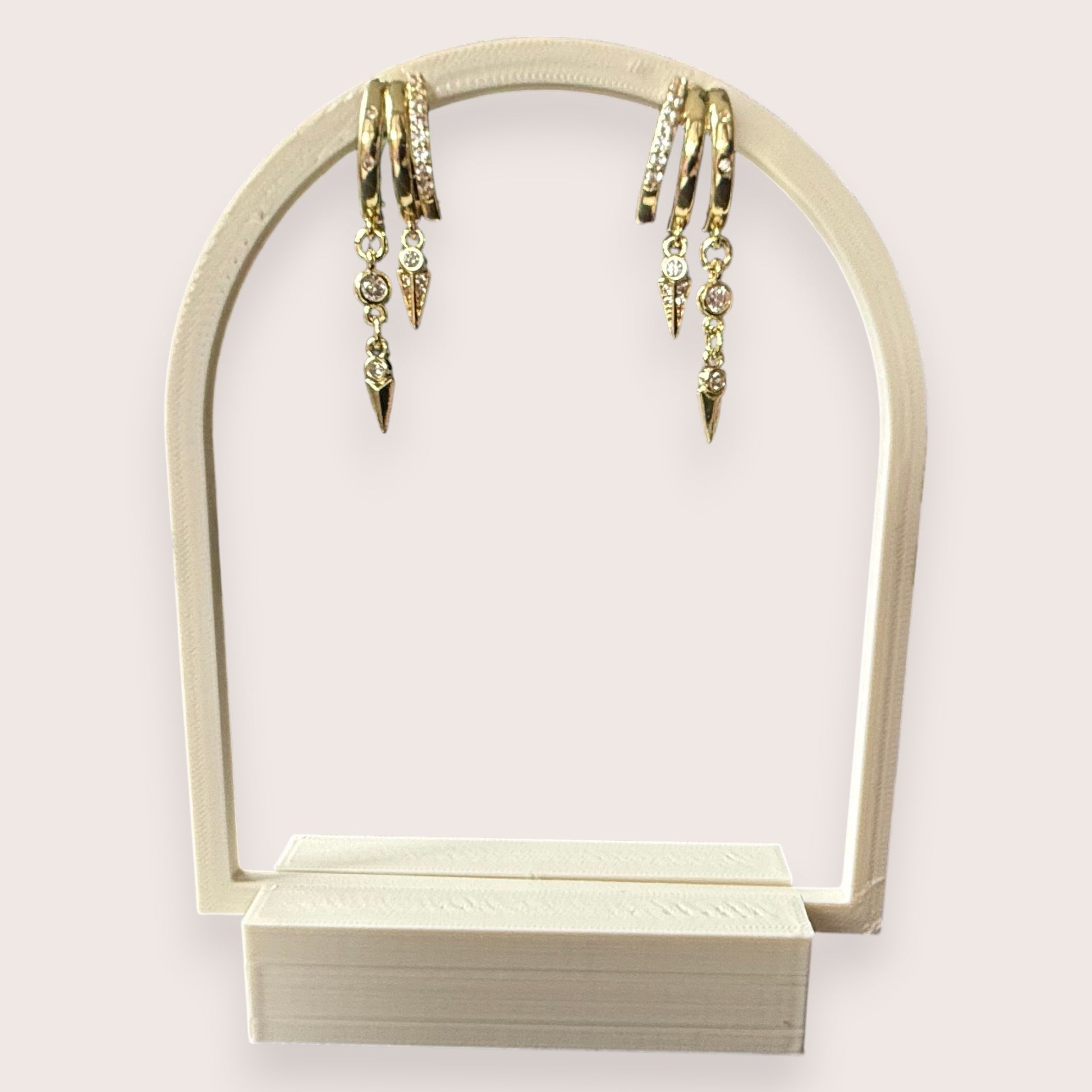 Nitelief gold hoop earrings with dangling crystal-encrusted spike charms displayed on a white arch stand