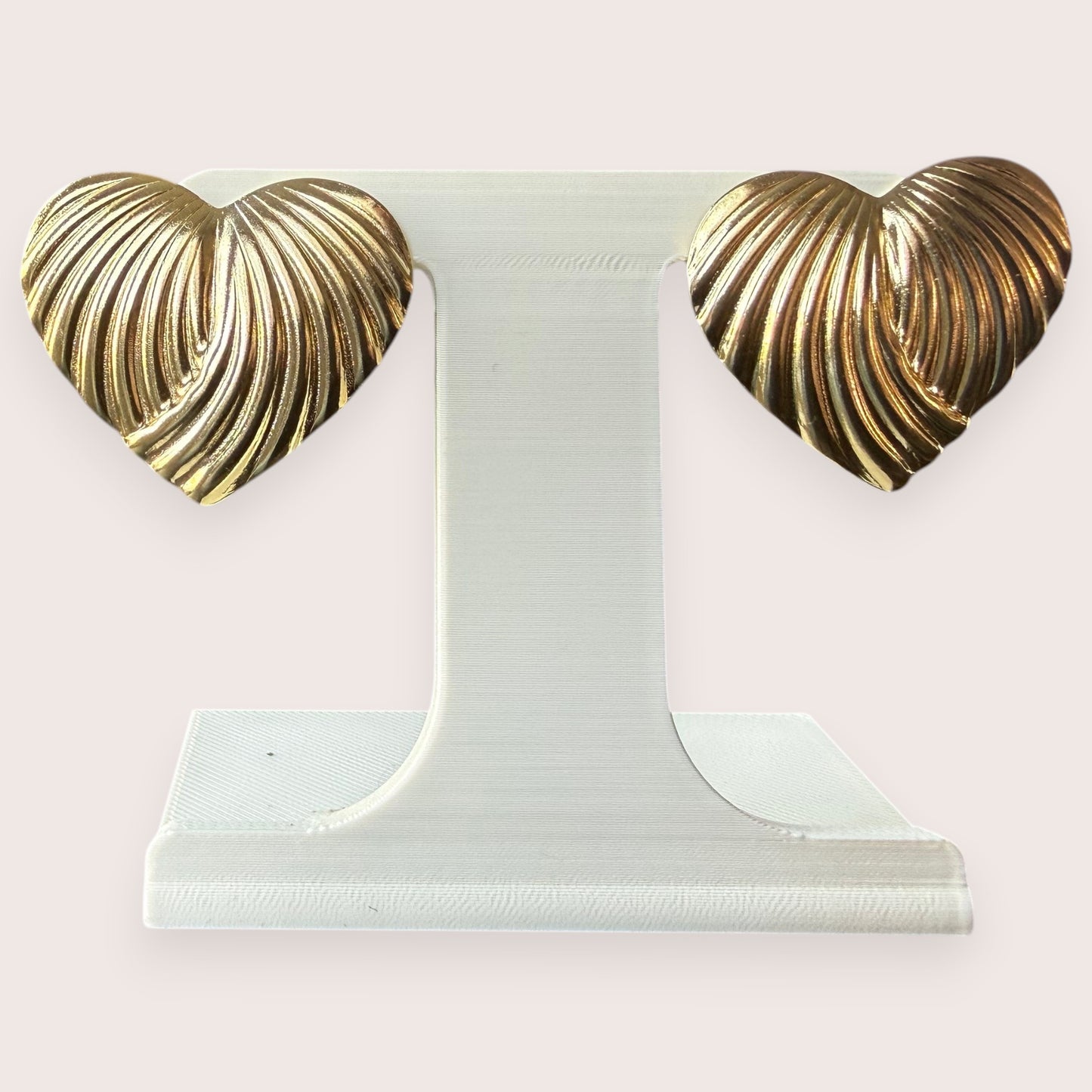 Nitelief CONCEPT golden heart earrings with a textured ribbed design on a white display stand