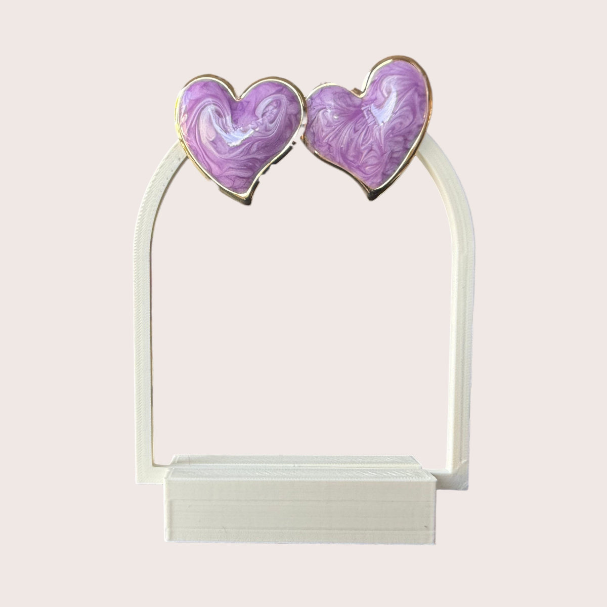 Nitelief pair of purple heart-shaped earrings with a marbled resin finish and gold-tone metal trim on a white stand