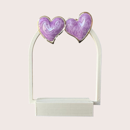 Nitelief pair of purple heart-shaped earrings with a marbled resin finish and gold-tone metal trim on a white stand