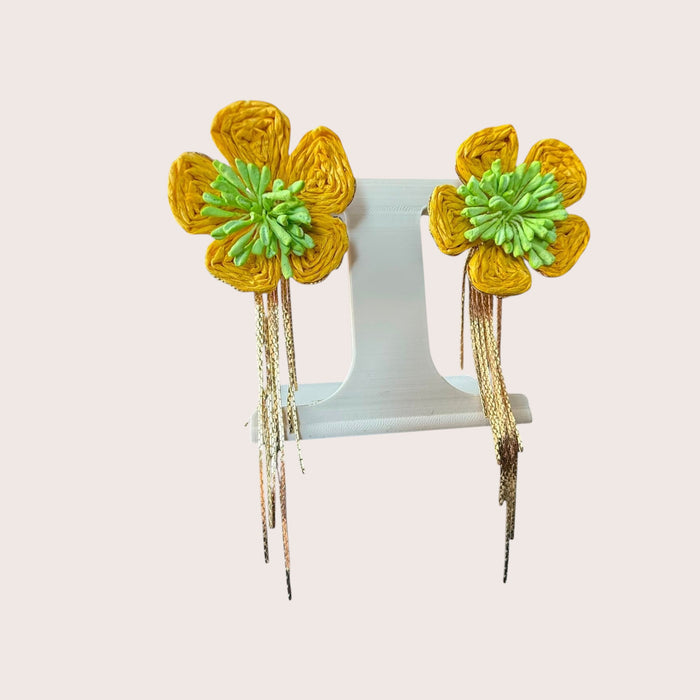 Nitelief Soleil raffia flower earrings in yellow and green with dangling gold-tone chains on a display stand.