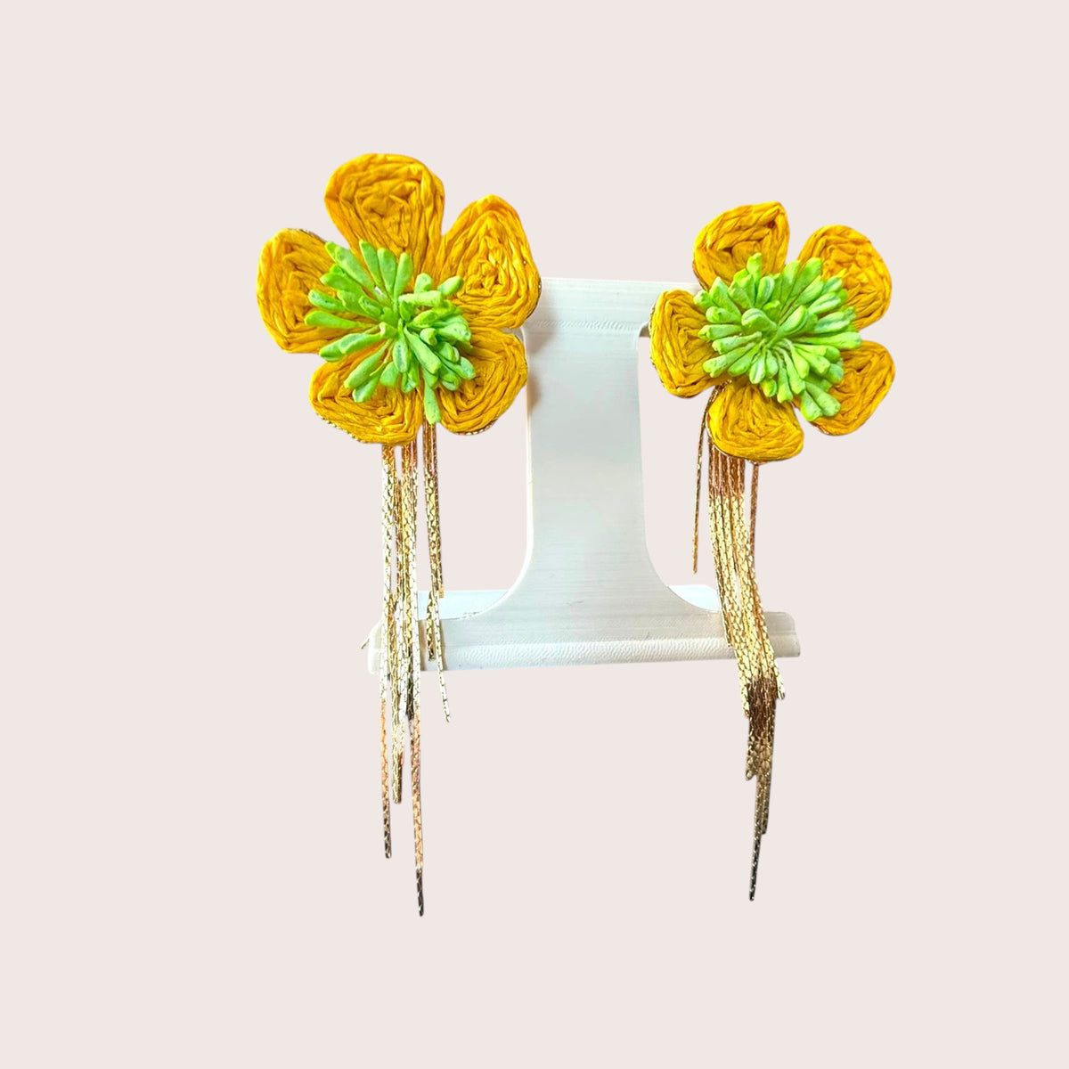 Nitelief Soleil raffia flower earrings in yellow and green with dangling gold-tone chains on a white display stand.