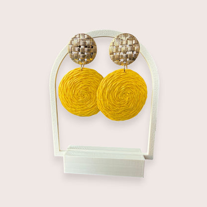 Nitelief CONCEPT Zonnetje yellow raffia circle earrings with gold-tone woven stud tops on a white display stand.